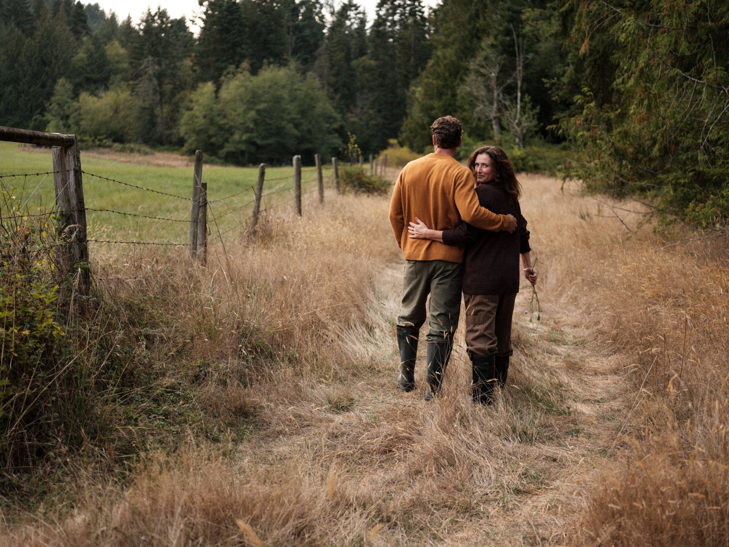 Two people walking together on a path in a natural setting with trees and grass.