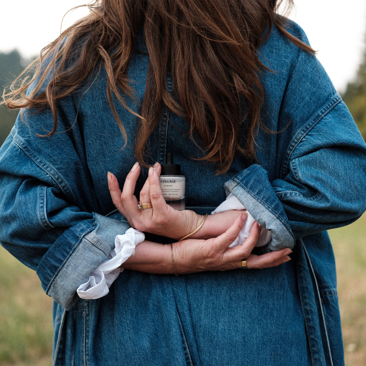 Person wearing a blue denim jacket holding a bottle of skincare